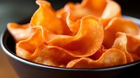 Crispy orange sweet potato chips in black bowl on dark background. Healthy vegetable snack food for diet and nutrition concepts.