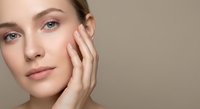 Young Caucasian woman with natural makeup touching face gently, showcasing healthy glowing skin and beauty routine for skincare and cosmetic products.