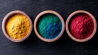 Vibrant yellow, green, and red powder pigments in wooden bowls arranged on dark slate background, natural colorful spices and dyes for art and cooking.