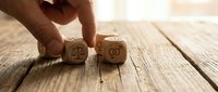 Hand placing wooden dice with justice scales and gender symbols on rustic wood surface representing legal equality and rights concepts.