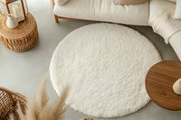 Cozy round white fluffy rug in modern minimalist living room with wooden furniture and natural decor elements creating warm aesthetic atmosphere.