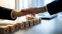 Business handshake over wooden blocks with checkmarks symbolizing successful partnership agreement and completed tasks in modern office setting.
