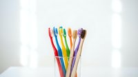 Colorful toothbrushes in glass holder on white background for dental hygiene and oral care routine.