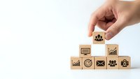 Hand placing wooden cube with team icon on stack of business symbol blocks representing leadership and human resources management concepts.