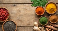 Colorful spices and superfoods in wooden bowls on rustic table. Turmeric, paprika, chia seeds, goji berries, ginger root creating healthy cooking ingredients flat lay.