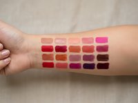 Colorful lipstick swatches displayed on woman's arm showing various shades from nude to deep burgundy for cosmetic testing and color selection.