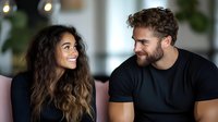 Young diverse couple sharing intimate moment, laughing together on sofa. Mixed race woman with long curly hair and bearded caucasian man in black t-shirt enjoying conversation.