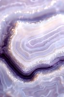 Purple and white agate crystal macro with golden glitter details, showing natural mineral layers and formations in ethereal dreamy tones. Suitable for luxury design.