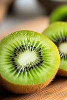 Fresh juicy kiwi fruit cut in half showing bright green flesh and black seeds on wooden surface, macro close up view with selective focus and natural lighting.