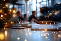 Modern office workspace with laptop computer and financial charts during festive season with warm bokeh lights creating professional holiday atmosphere.