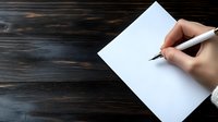 Hand holding white pen poised to write on blank paper against dark wooden table background, ready for creative writing or note-taking.
