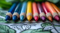 Colorful wooden pencils arranged in rainbow order lying on adult coloring book page with floral pattern, macro shot showing pencil tips and texture details.