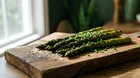 Fresh green asparagus spears seasoned with herbs on rustic wooden cutting board in bright kitchen setting for healthy cooking and meal preparation.