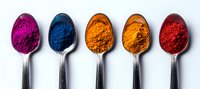 Vibrant colorful powder pigments in silver spoons arranged in row showing pink, blue, orange and red hues against white background, macro photography.