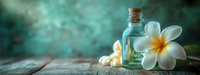 Spa composition with plumeria flowers and aromatherapy oil in turquoise glass bottle on wooden surface against blurred teal background. Wellness concept.