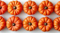 Fresh orange pumpkins arranged in neat rows on white background, top view. Seasonal autumn harvest pattern for Halloween and Thanksgiving decor.