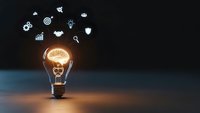 Glowing light bulb with brain filament surrounded by business innovation icons on dark background representing creative thinking and entrepreneurship.
