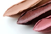 Macro shot of lipstick swatches in nude, burgundy and pink shades on white background showing creamy texture and color pigments for beauty and cosmetics.