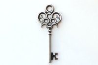 Vintage ornate silver key with decorative heart-shaped bow and scroll design isolated on white background, suitable for jewelry making and decorative elements.