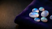 Collection of iridescent opal gemstones displaying rainbow colors on dark purple velvet fabric surface for jewelry making and luxury accessories design.