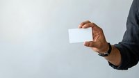 Male hand holding blank white business card against neutral background. Ideal for corporate branding and professional networking designs.