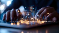 Modern cityscape with glowing bokeh lights reflecting on laptop screen, showing urban nighttime skyline with illuminated skyscrapers and business buildings.