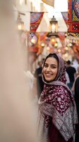 Young Middle Eastern woman wearing traditional burgundy headscarf smiling in colorful marketplace with lanterns and textiles creating warm atmospheric shopping scene.