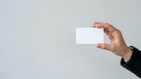 Caucasian male hand holding blank white business card against neutral gray background, suitable for branding and corporate identity mockups.