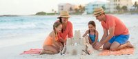 Happy family of four building sandcastle together on tropical beach during summer vacation. Parents and children enjoying quality time by ocean shore.