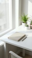 Minimalist white desk workspace with closed notebook, pen and small potted plants by bright window. Clean modern home office setup for productivity and focus.
