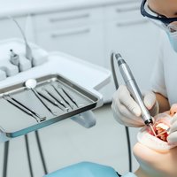 Dentist performing oral examination with dental tools in modern clinic. Professional healthcare worker treating patient in sterile medical environment.