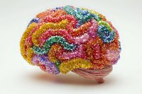 Colorful crystal-encrusted anatomical brain model featuring vibrant rainbow hues of pink, yellow, blue, and red glitter texture on white background, isolated for creative projects.