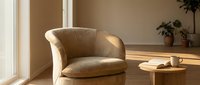 Comfortable beige upholstered armchair in minimalist interior with wooden side table, potted plants, and natural sunlight for home decor and furniture design.