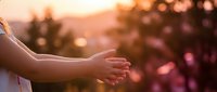 Person extending open hands in warm golden sunset light with blurred nature background creating peaceful spiritual moment for meditation and mindfulness concepts.