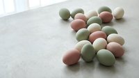 Colorful pastel Easter eggs in soft pink, green and cream tones scattered on neutral textured surface for spring holiday decorating and seasonal celebrations.