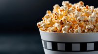 Fresh popcorn overflowing in classic striped bowl against dark background, dramatic side lighting creates contrast between kernels and shadows. Movie snack concept.