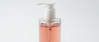 Liquid soap or gel cleanser in clear pump bottle with pink or coral colored formula on white background, isolated for product packaging and cosmetic design use.