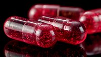 Transparent red capsules with glittering particles inside on reflective black surface, used in pharmaceutical or supplement industry.
