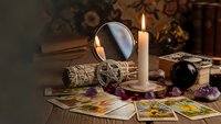 Mystical fortune telling setup with tarot cards, crystal ball, candle and sage bundles on wooden table creating atmospheric divination scene.