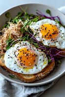 Sunny side up eggs on toasted bread garnished with black sesame seeds, microgreens and purple cabbage, served with noodles on white ceramic plate.