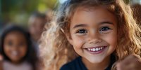 Cheerful mixed-race girl with curly hair and bright smile looking at camera, natural outdoor lighting creates warm atmosphere for childhood portraits.