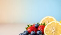 Fresh mixed berries and lemon slices on pastel gradient background for healthy eating, nutrition concepts, smoothie recipes and summer refreshment.