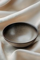 Minimalist ceramic bowl with speckled gray glaze on cream silk fabric background, creating elegant contrast and texture for modern tableware styling.