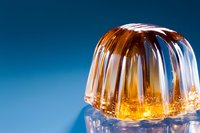 Golden jelly dessert with ribbed dome shape on reflective surface against blue background, showcasing translucent texture and light play for food photography.