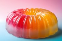 Colorful layered gelatin dessert in ring shape transitioning from red to orange, set on blue background. Sweet treat with gradient effect and soft lighting.