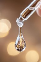 Macro shot of cosmetic serum or essential oil drop with golden bubbles falling in transparent liquid against blurred warm bokeh background.