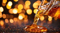 Amber liquid pouring from bottle creating splash with golden bokeh lights background, luxury beverage photography with festive atmosphere.