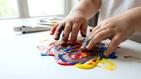 Child hands creating colorful finger painting artwork on white paper with red blue yellow paint for creative art education and sensory play activities.