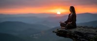 Woman meditating on mountain cliff during golden sunset with layered hills in background. Peaceful mindfulness and spiritual wellness concept for relaxation content.