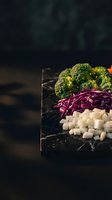 Fresh broccoli, purple cabbage and white beans arranged on dark marble surface for healthy cooking and meal preparation.